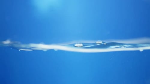 Waves of crystal clear blue mineral water, creating some tiny bubbles and droplets of in a water tan