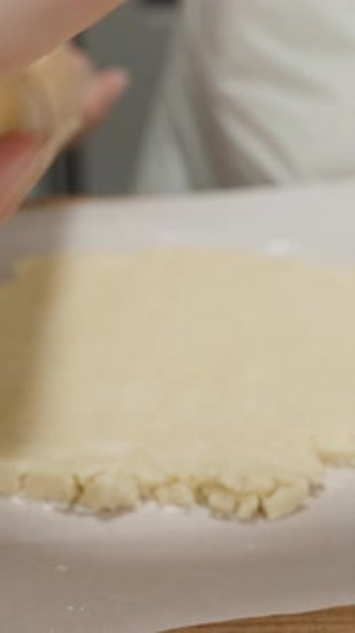 Vertical video. The woman in a white apron rolls out the dough with a wooden rolling pin.