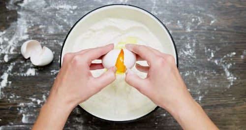 Hands Cracking an Egg into Flour in Bowl