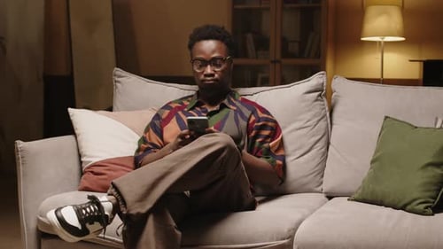 Man Relaxing on Couch Using Smartphone at Night