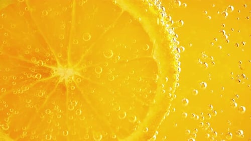 Une tranche d'orange mûre dans des bulles d'eau sur fond orange.