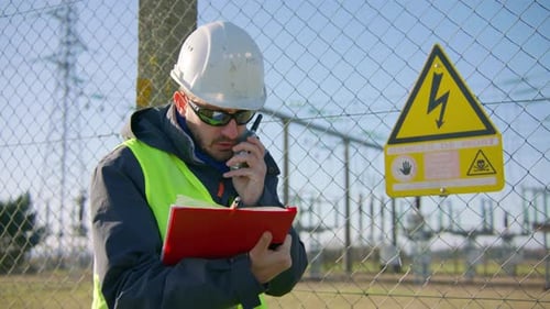 Male engineer talking over the radio while holding a clipboard at the electric substation, handheld