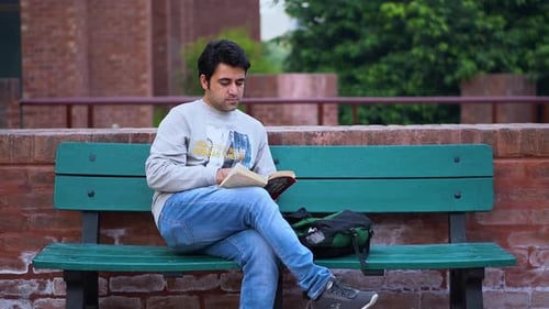 Männlicher Bücherwurm genießt die Natur beim Lesen, junger südasiatischer Mann vertieft sich in das Lesen im Freien.