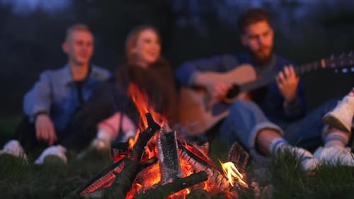 Friends Gathered Around Campfire at Night With Guitar