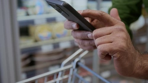 Man using Phone in Supermarket Swiping Screen Checking Shopping List