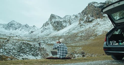 Homem autônomo acampando sentado na épica vista da montanha usando laptop em uma viagem