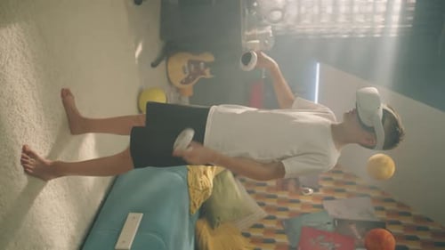 Teenage Boy with VR Headset and Joysticks Plays Games in His Room Makes Gestures