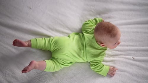Top View of Cute Adorable Newborn Baby Wearing Yellow Cotton Bodysuit Lying on Stomach on White