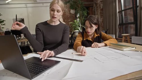 Female Architect Team Collaborating on Laptop and Floor Plan in Modern Office