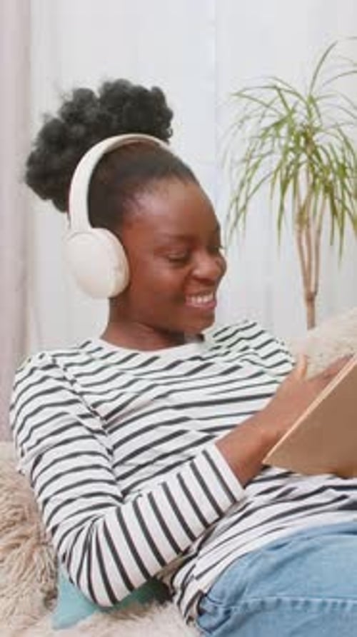 Afroamerikanerin, junger Erwachsener, liest Roman, sitzt konzentriert auf dem Sofa und entspannt sich zu Hause