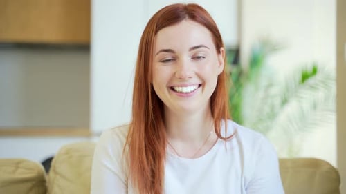 Close-up portrait of a redhaired young happy girl or woman happily smiling in living room at home.