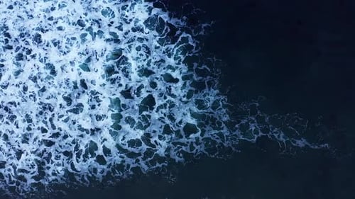 Straight down aerial view of a wave breaking with bubbles and sea foam creating an abstract white wa