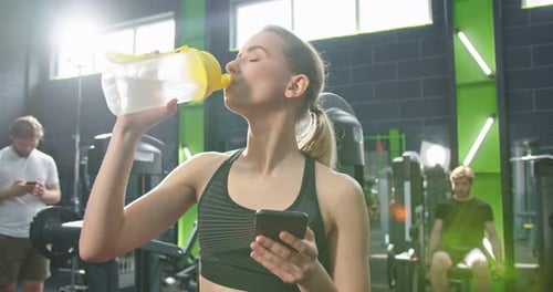 Portrait View of the Strong Woman Looking at the Smartphone Screen and Drinking a Lot of Water After