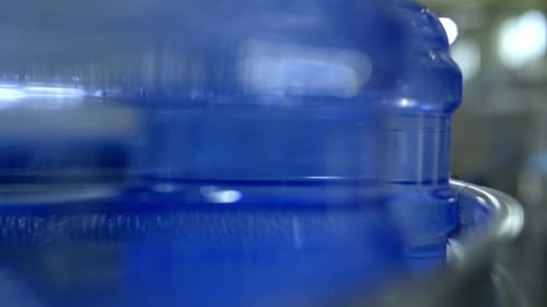 A close-up view of water containers in a production line.
The focus on the sleek blue bottles.
8k