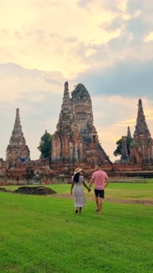 un homme et une femme marchent dans un champ d'herbe devant un temple Ayutthaya Thaïlande