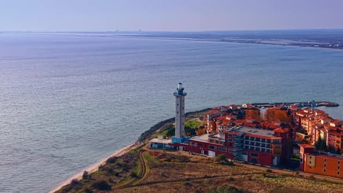 Distancing from the square-towered lighthouse adjacent to the colorful house complex.