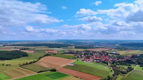 The scene shows a small village surrounded by green fields and farmland.
