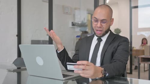 Frustrated Man Using Credit Card and Laptop in Office