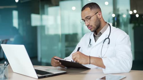 Focused Doctor Writes on Clipboard in Modern Office