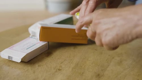 Person Opening Pill Container on Wooden Table