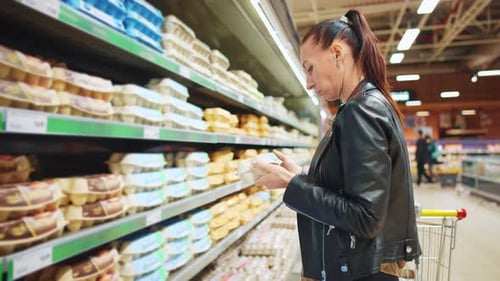 Young Beautiful Woman Stands in Grocery Store and Chooses Products on Supermarket Shelves Girl Looks