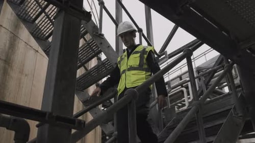 Industrial Worker Descends Metal Staircase Outdoors on Overcast Day