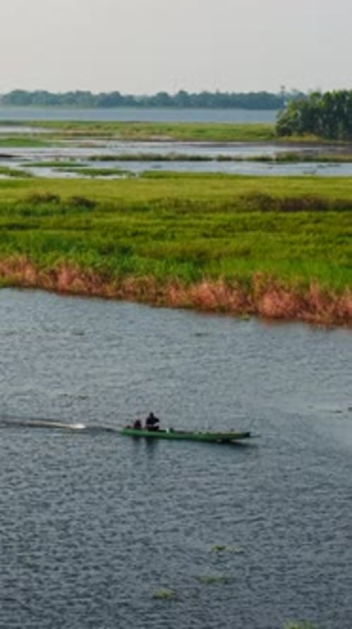 Un pêcheur conduit un petit bateau sur une rivière calme près d'une large rive verdoyante