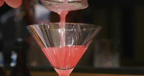 De perto, um barman profissional está servindo um coquetel alcoólico com cubos de gelo para os clientes