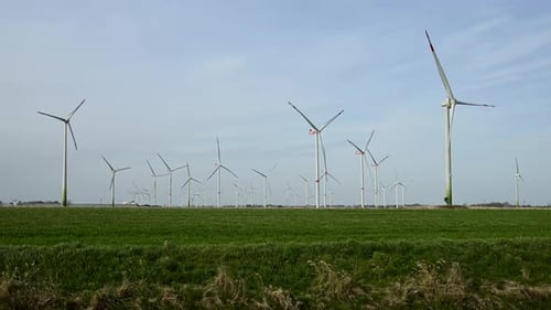 Vue large de plusieurs éoliennes en rotation en pleine campagne sous de légers nuages, mettant en valeur