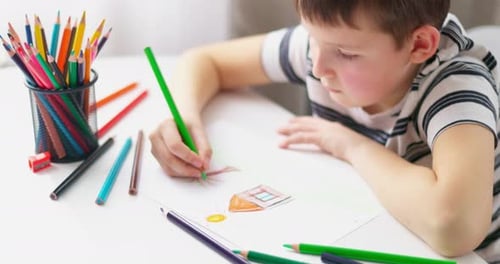 Netter Junge, der zu Hause oder im Klassenzimmer mit Farbstiften auf ein Blatt Papier zeichnet