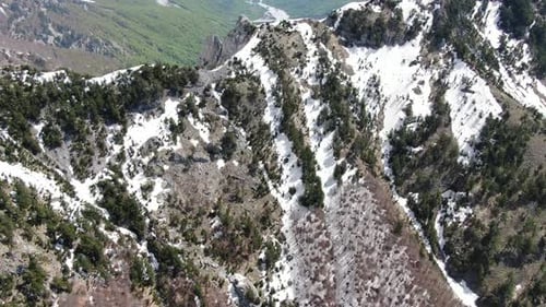 Vue par drone en Albanie survolant les Alpes montrant un sommet enneigé et rocheux entre deux f verts