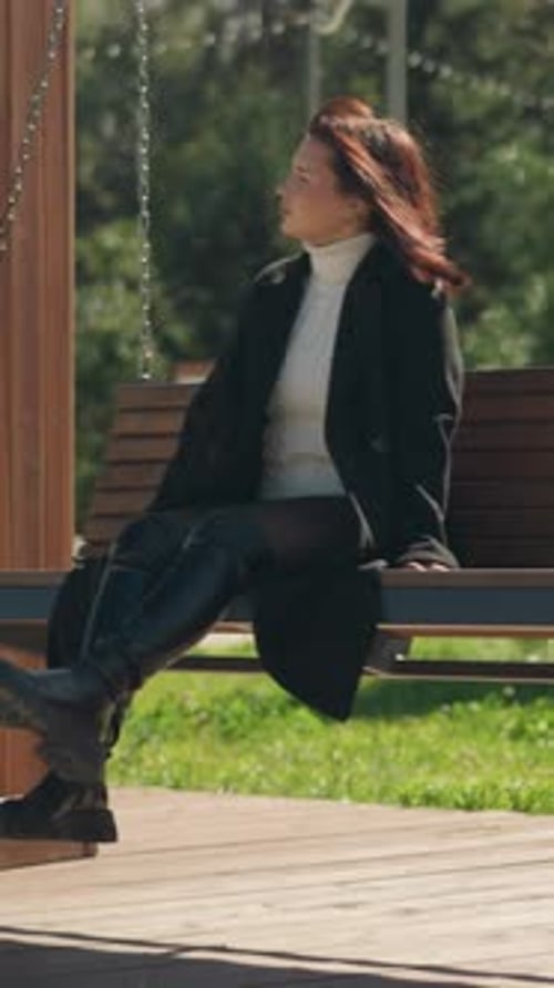 Lady in Black Coat on Wooden Swing in Green Park Setting