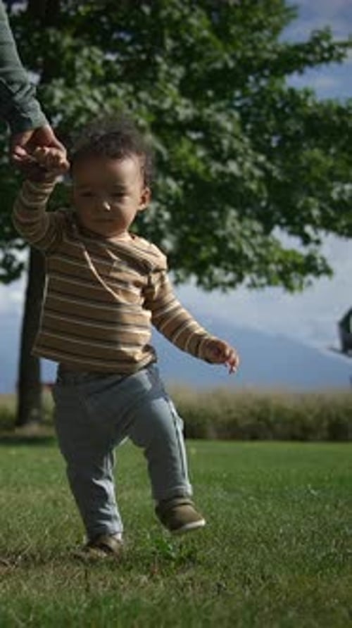 Baby Taking First Steps Outside with Parent