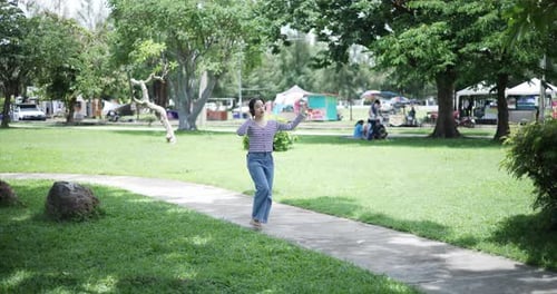 Happy Asian woman wearing wireless headphones enjoying listening to music in fresh air in a park