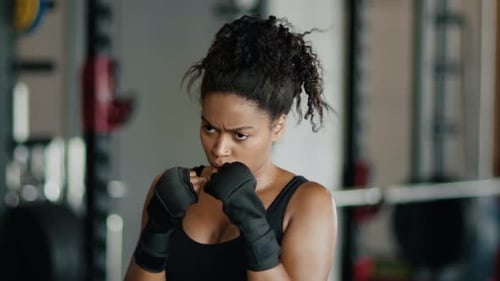 Junge starke aktive Afroamerikanerin Kickboxen im Fitnessstudio Punching Forward mit eingewickelten Bändern