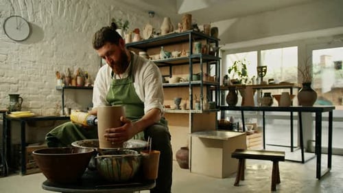 A potter works in a pottery workshop drying a raw clay pot with an electric dryer