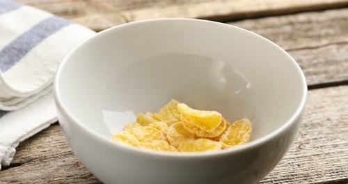 Cereal Pours into White Bowl on Wooden Surface
