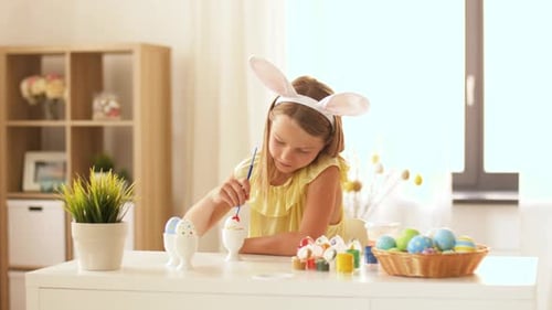 Fröhliches junges Mädchen mit Hasenohren färbt im Frühling Ostereier zu Hause