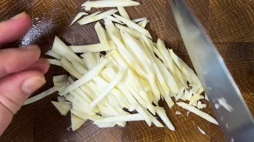 A cook chops parsley root with a knife on a wooden cutting board.