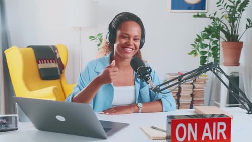Jovem apresentadora de rádio afro-americana canta no ar sentada perto do microfone