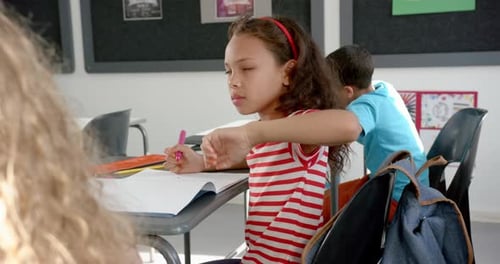 In school, girl in striped shirt sitting at desk, holding backpack