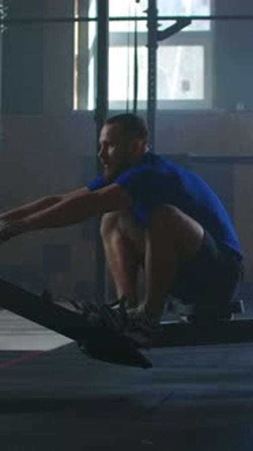 Focused Athlete Training on Indoor Rowing Machine in Dimly Lit Gym Demonstrating Strength Endurance