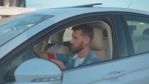 Man Sits in Car Looking at Phone