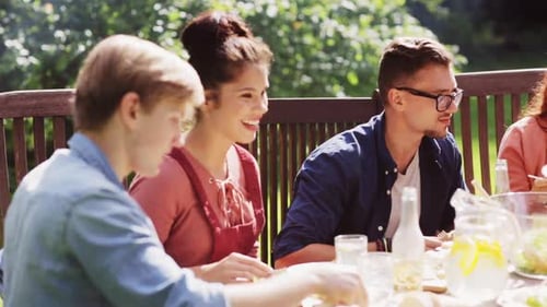 Happy friends enjoying summer garden party dinner with food and drink