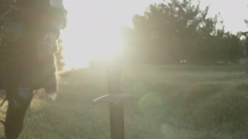 A Man in a Medieval Knight Costume Approaches a Sword Stuck in the Ground in the Bright Rays of
