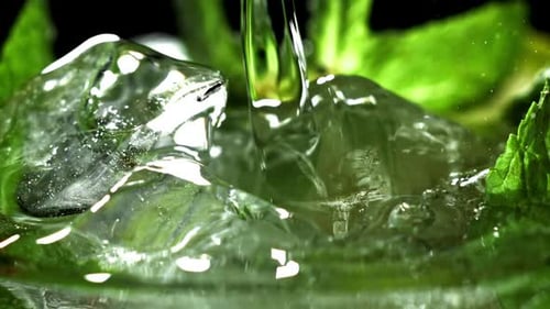 Water being poured over ice and mint leaves