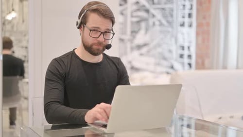 Young Adult Man with Headset Looking toward Camera in Call Center