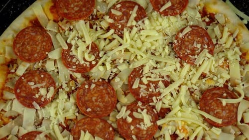 Topdown aerial of an uncooked pepperoni pizza, with a tomato base and lots of grated cheese.