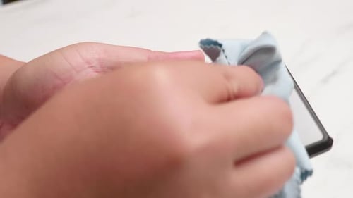 Close-up of a person cleaning up her smart mobile phone with a clean blue washcloth.
