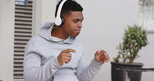 African American man wearing hoodie tapping to beat on patio, conducting and adjusting headphones